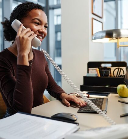 Side view portrait of black young businesswoman answering phone calls at desk in office and smiling
