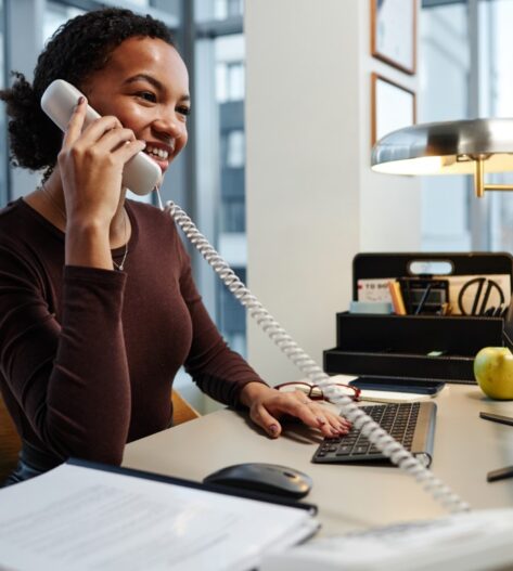 Side view portrait of black young businesswoman answering phone calls at desk in office and smiling